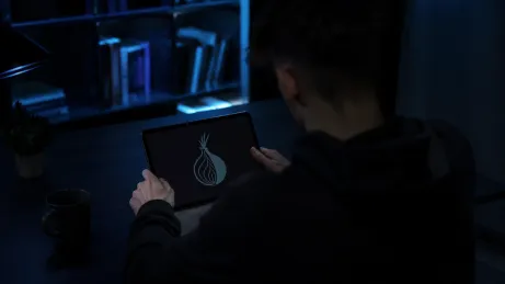 A user is closely examining the Hidden Wiki logo on a tablet in a dimly lit room.